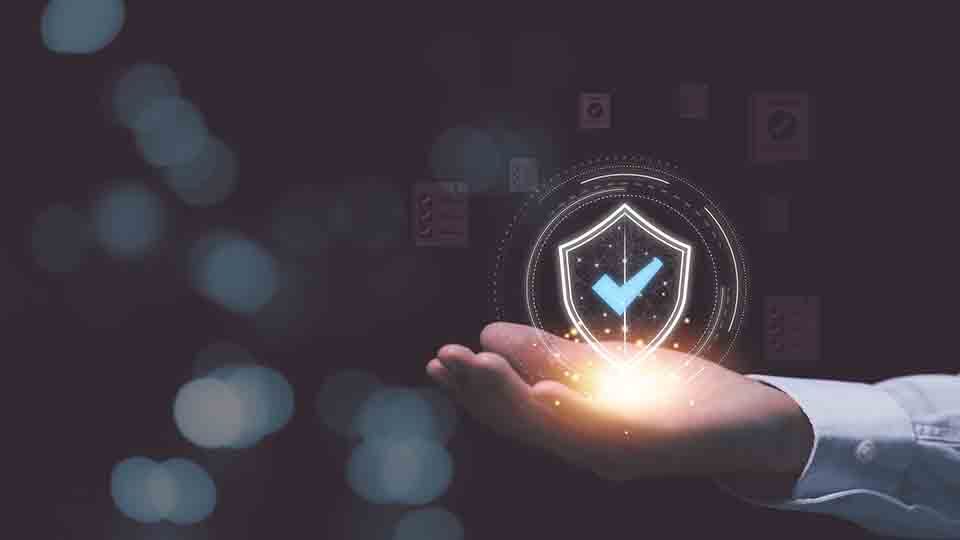 Hand presenting a luminous digital security shield with checkmark icon against a dark tech background
