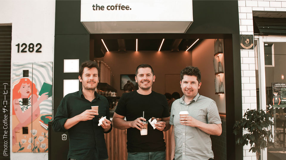 Photo of the Fertonani brothers, Alexandre, Carlos, and Luis, standing outside one of their coffee shops each holding a coffee to go.