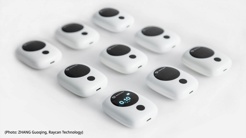 Photo of nine black and white RAYCAN personal radiation detectors arranged on a white surface