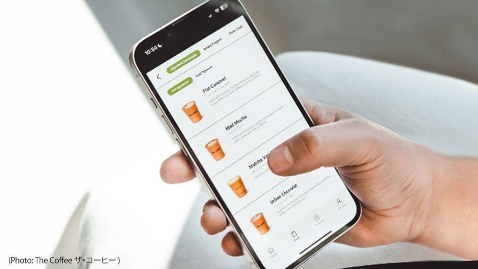 Photo features a hand holding a smart device with The Coffee ザ・コーヒー's app menu diplayed.