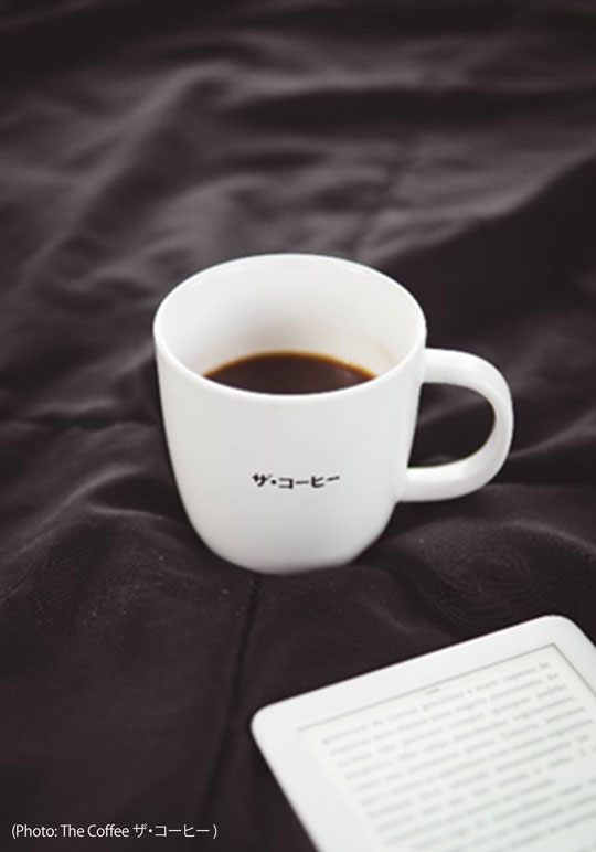 Visual features a white cup filled with black coffee and a white electronic reading device. ザ・コーヒー is written on the cup.