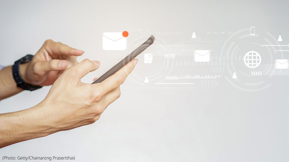 Visual shows a closeup shot of a business person's hand, using a touch screen on a smartphone device to send email