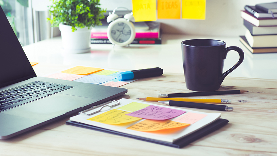 A laptop, a notepad with sticky noted and a cup on a worktable