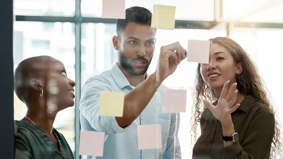 Colleagues brainstorming with sticky notes on a glass wall